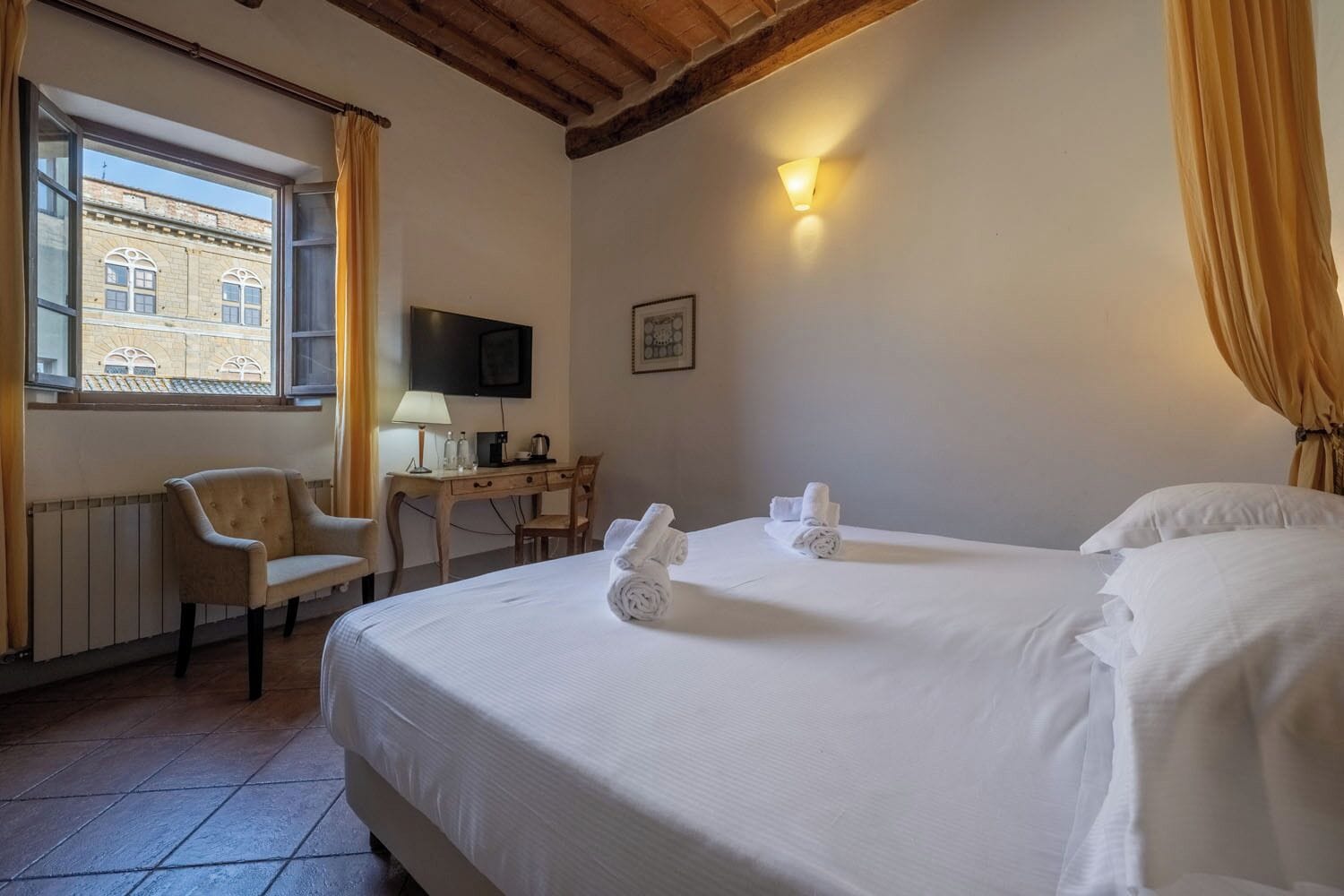 A hotel room with two beds, a desk with a chair, a television, and a window with curtains.
