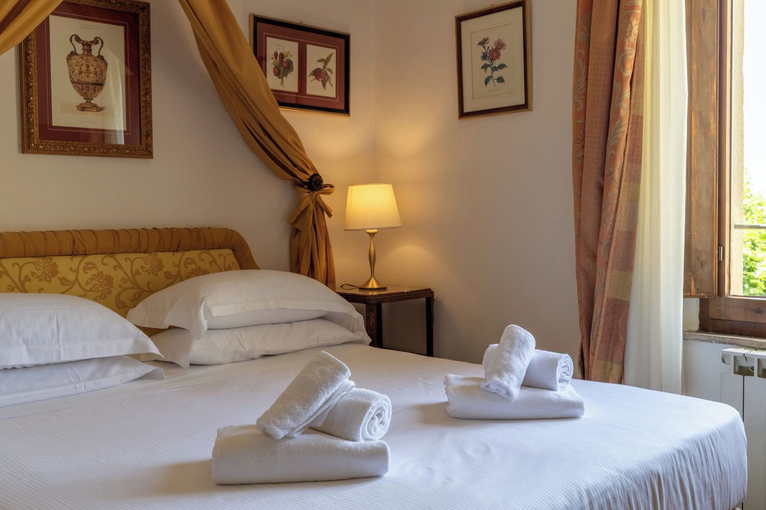 A hotel room with a bed, pillows, a lamp, and a window with curtains.