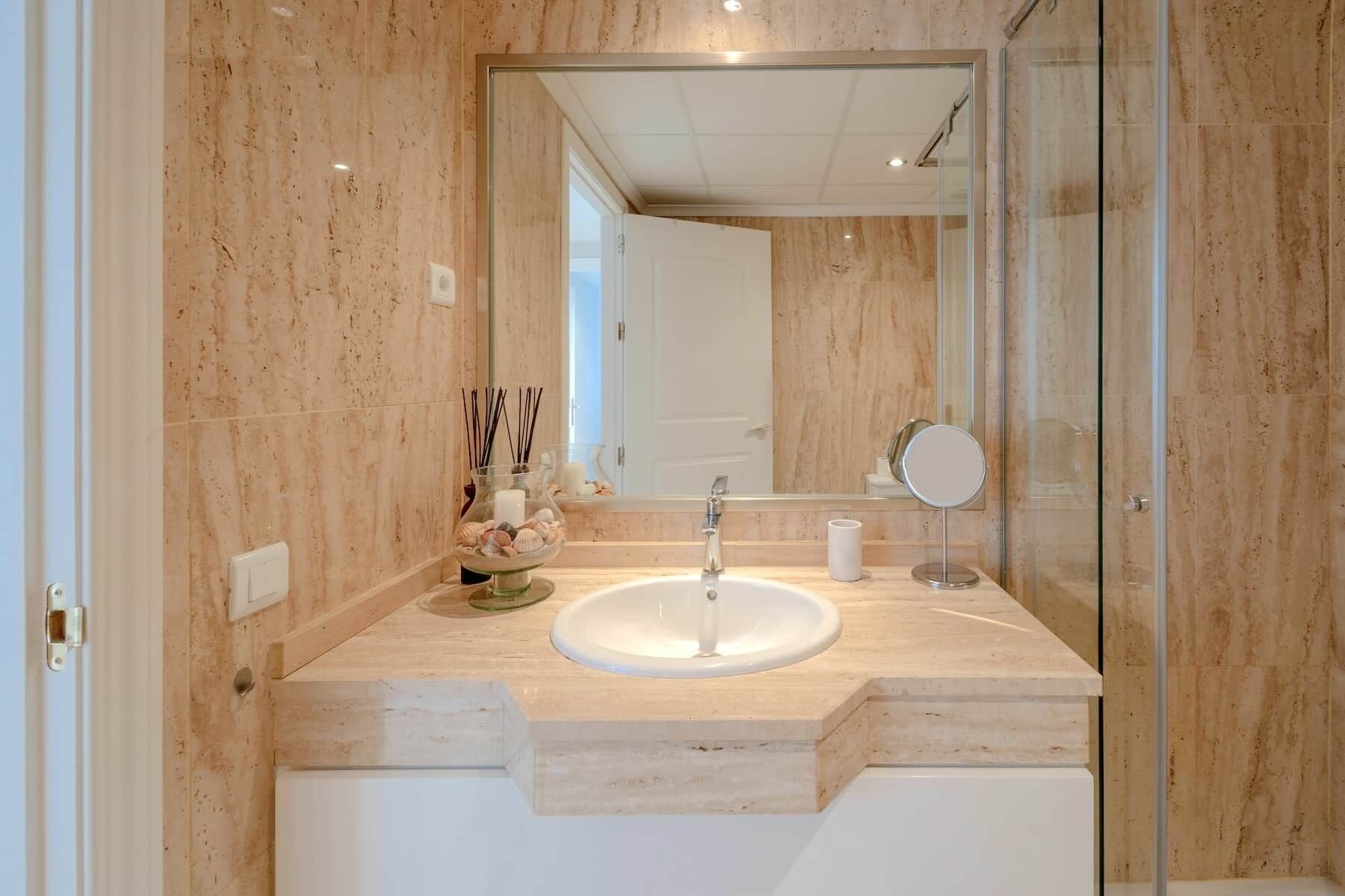 A bathroom with a marble countertop, a sink, a mirror, and a glass shower enclosure.