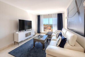 Ein modernes Wohnzimmer mit Flachbildfernseher, einem weißen Sofa, einem Couchtisch und einem großen Fenster mit Vorhängen.