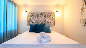 Ett hotellrum med en stor säng, ett dekorativt sänggavel, två kuddar, en väggklocka och en kompass som prydnad.