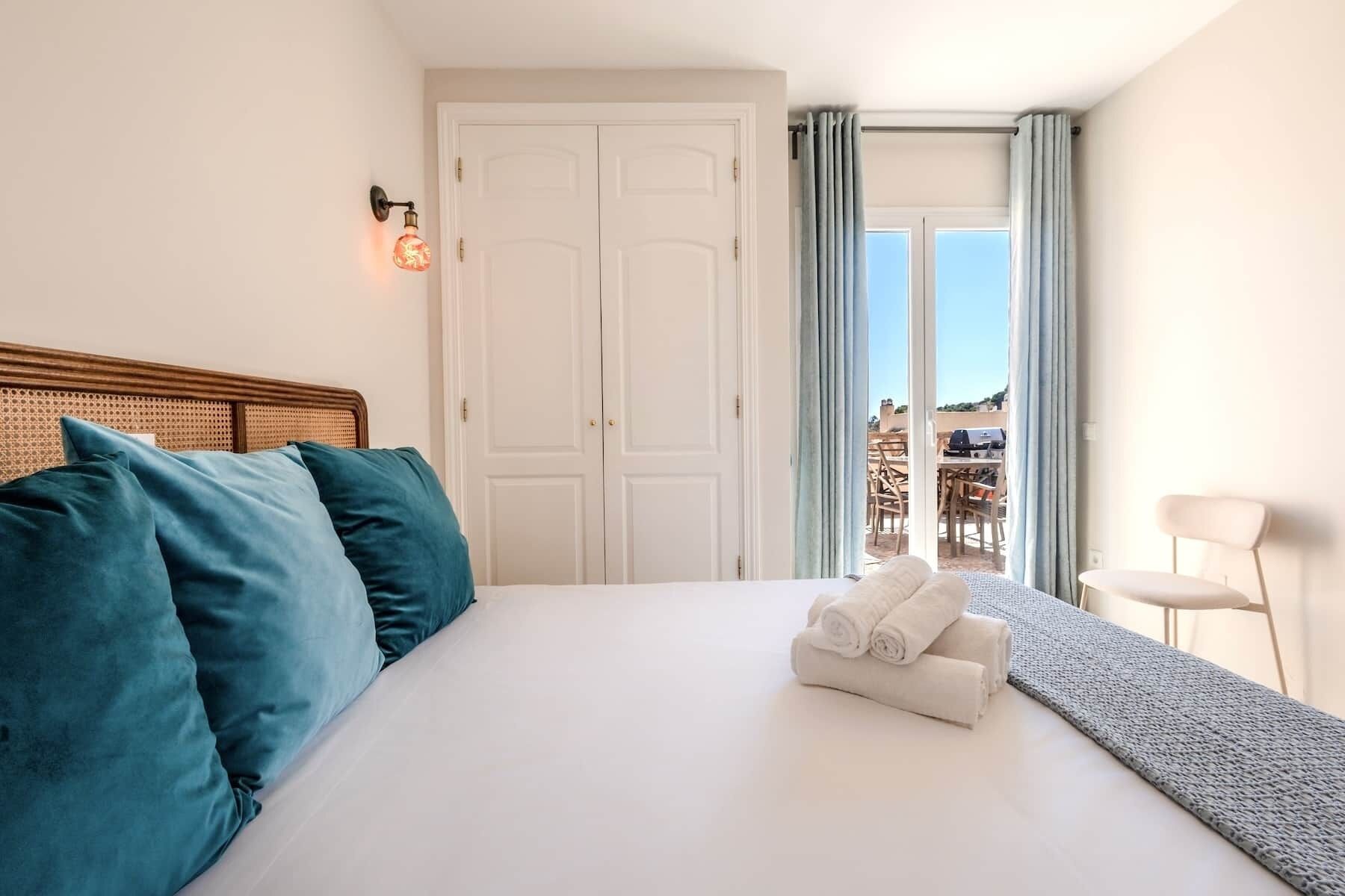 A hotel room with a bed, a door, a window with curtains, and a view of the outside.