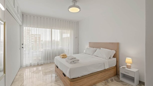 A hotel room with a bed, a bedside table with a lamp, a window with sheer curtains, and a ceiling light. - RDR568 - Charming 1 Bed Apt in Jardines del Mar (Marbella)