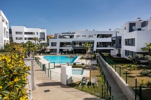 Ein modernes Wohngebäude mit Schwimmbad, Liegestühlen und einem gepflegten Garten.