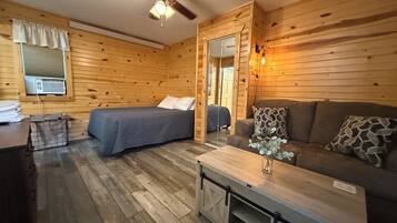 A room with a bed, a sofa, a small table, a ceiling fan, and a window with blinds.
