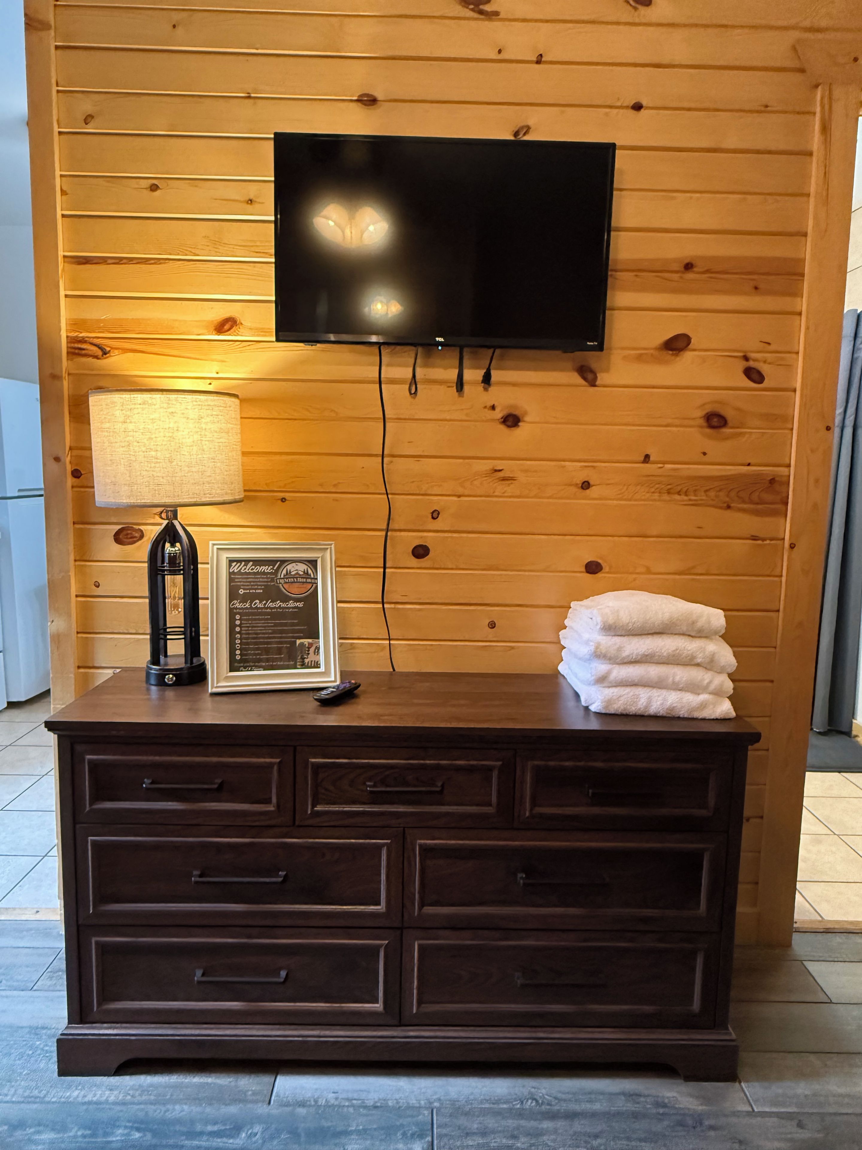 A wooden wall with a flat-screen TV mounted above a dark wooden dresser with drawers.