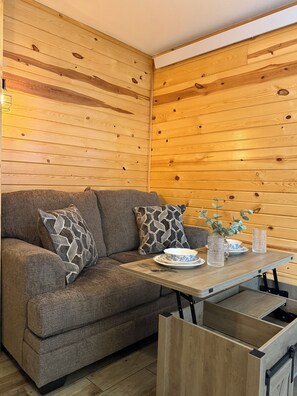 Una habitación con paneles de madera, un sofá, cojines estampados, una mesa con un cuenco y un jarrón.