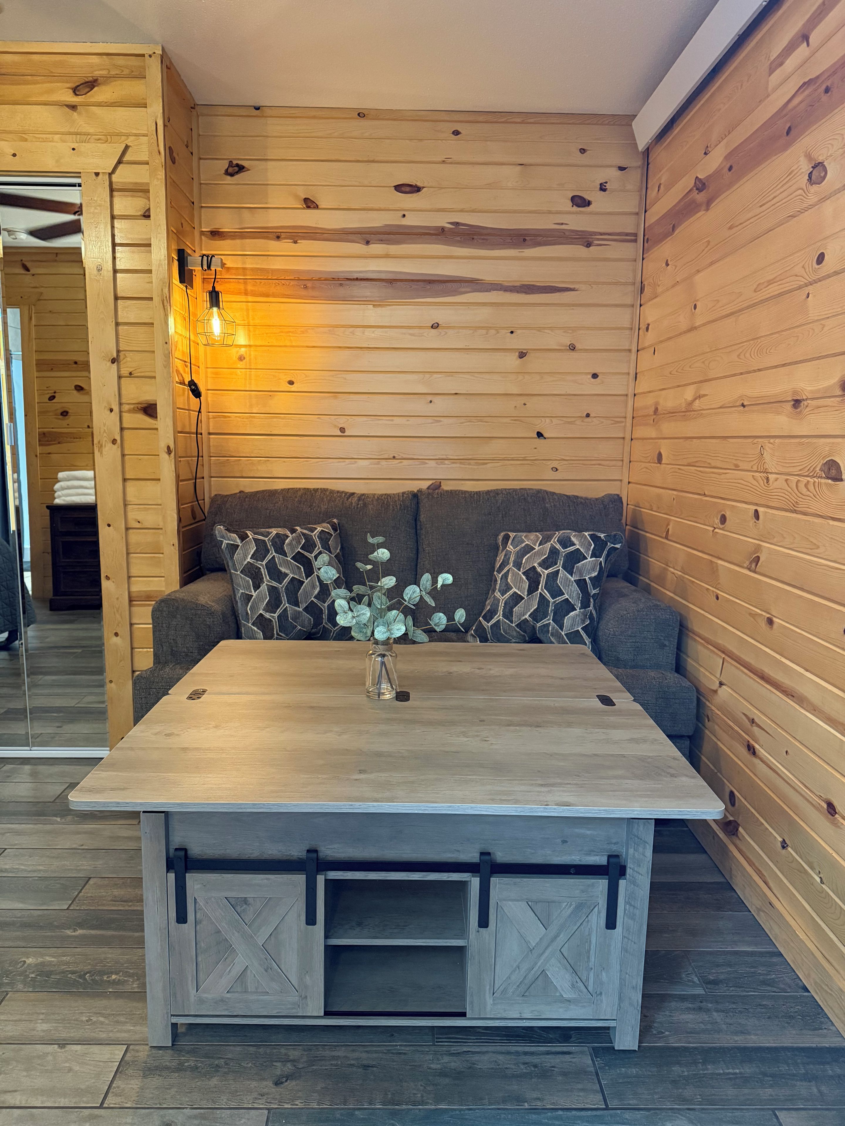 A wooden-paneled room with a sofa, a table with drawers, and a wall-mounted light fixture.