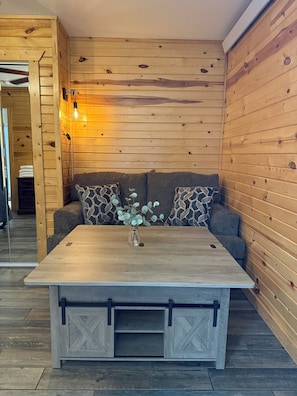 Una habitación con paneles de madera, un sofá, una mesa con cajones y una lámpara fijada en la pared.