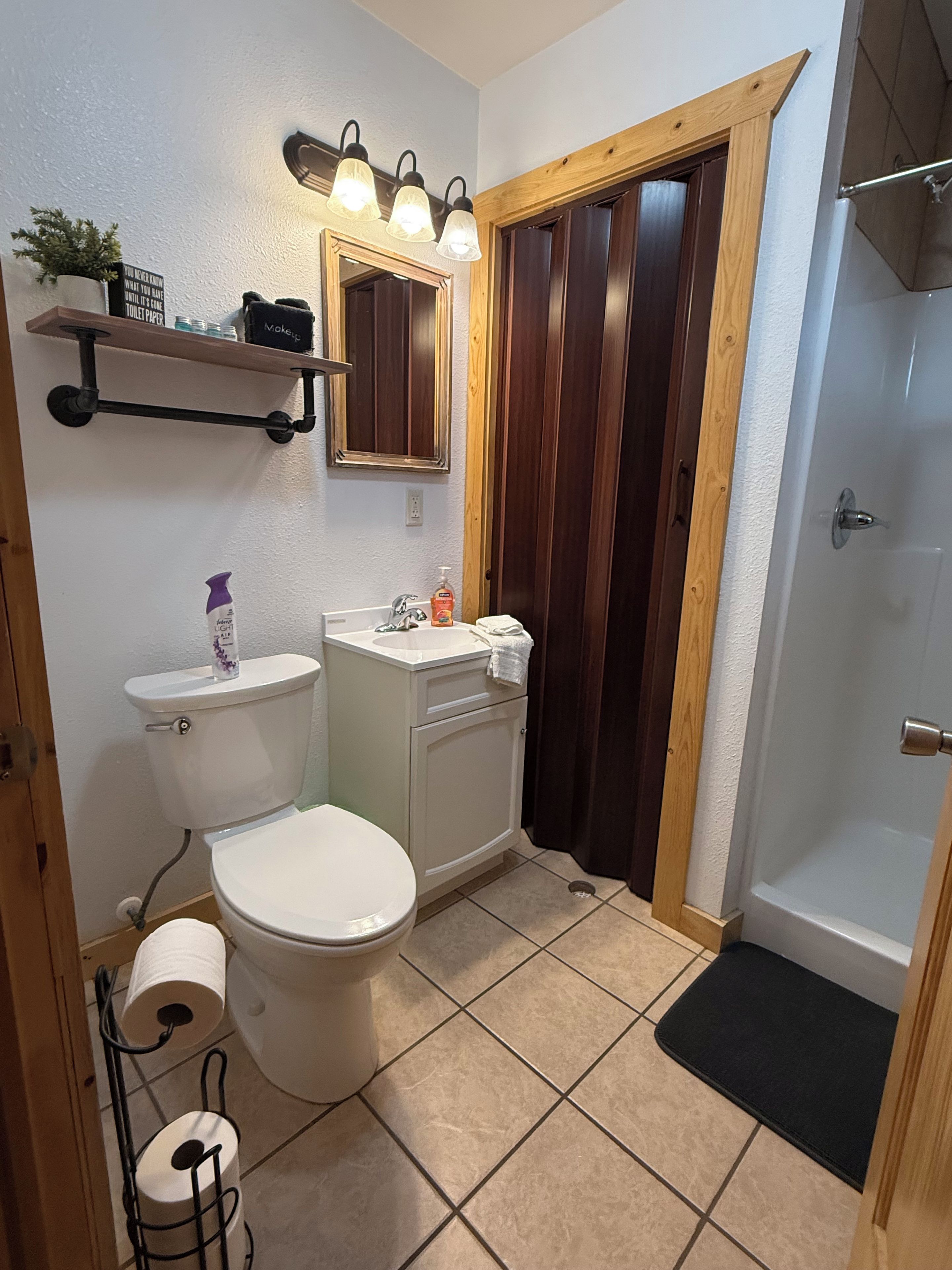 A bathroom with a toilet, sink, mirror, and shower area.