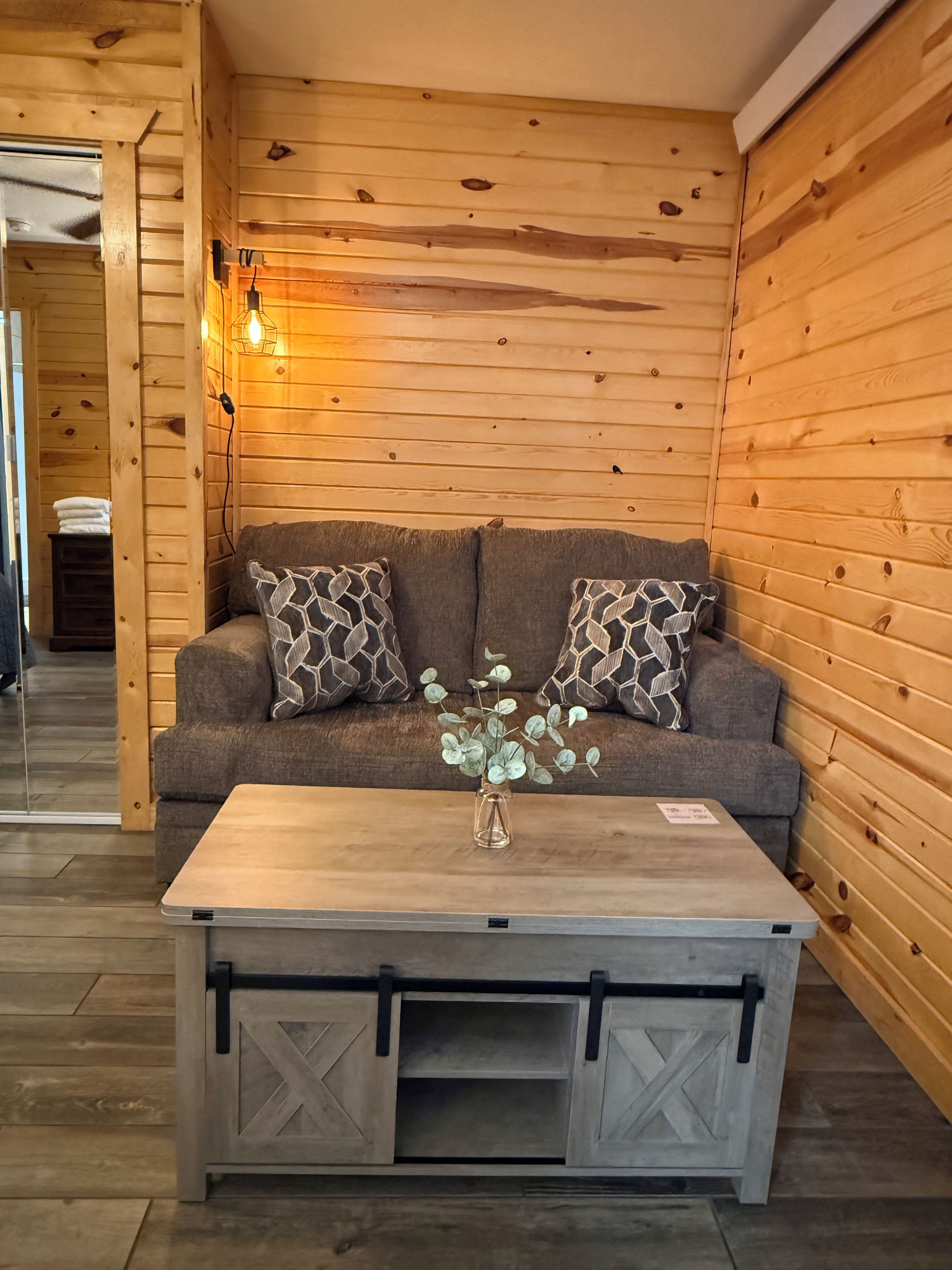 A cozy room with a wooden wall, a sofa with patterned cushions, a small table with a vase, and a sliding barn-style cabinet.