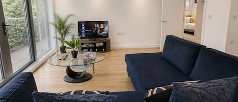 A modern living room with a dark blue sofa, a glass coffee table, and a flat-screen TV.