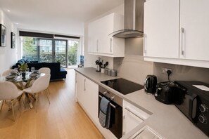 A modern kitchen with white cabinetry, a black induction cooktop, and a coffee maker. - Modern 2-Bedroom flat w/ AC & Balcony in Angel near King's Cros & Regent's Canal (London)