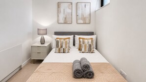Una camera da letto ordinata con un letto, cuscini, un comodino e una lampada.