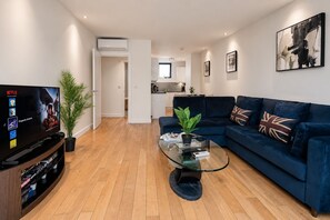 A modern living room with a flat-screen TV, a dark blue sofa, a glass coffee table, and a potted plant. - Modern 2-Bedroom flat w/ AC & Balcony in Angel near King's Cros & Regent's Canal (London)