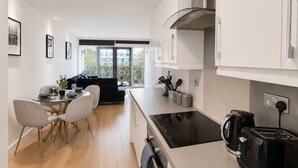 Eine moderne Küche mit einem schwarzen Induktionskochfeld, einer Kaffeemaschine und einem Toaster. Ein Essbereich mit rundem Tisch und Stühlen ist ebenfalls vorhanden.