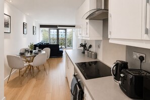 A modern kitchen with a black induction cooktop, a coffee maker, and a toaster. There is a dining area with a round table and chairs. - Modern 2-Bedroom flat w/ AC & Balcony in Angel near King's Cros & Regent's Canal (London)