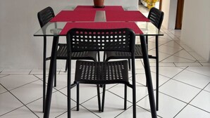 Un coin repas avec une table en verre, des chaises noires, un chemin de table rouge et une plante en pot.