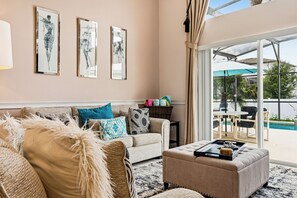 A living room with a sofa, ottoman, and a table with decorative items. There are three framed artworks on the wall. - 4 BDR South-Facing Disney Retreat (Kissimmee)