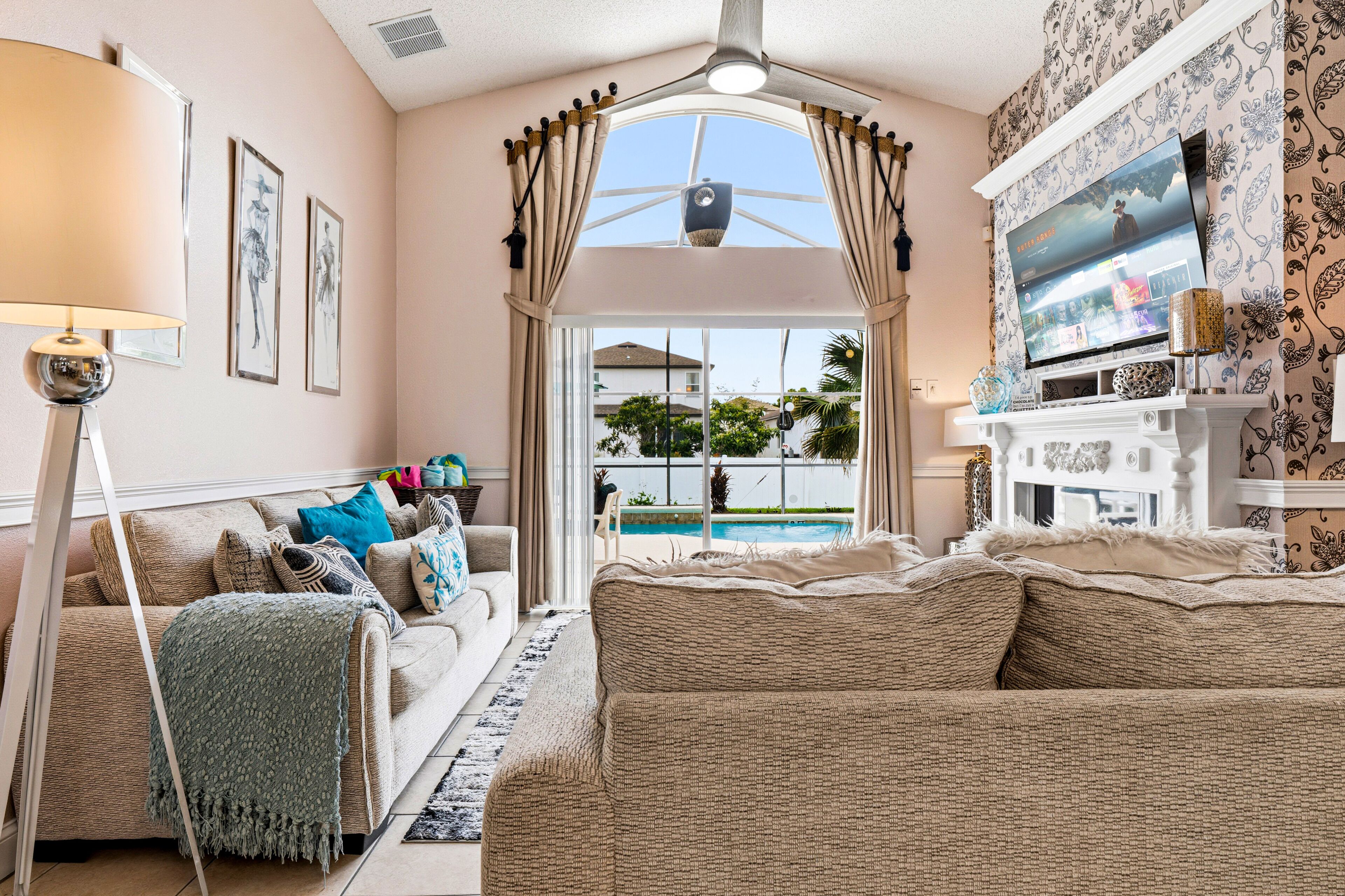 A living room with a sofa, a television, and a view of a swimming pool.