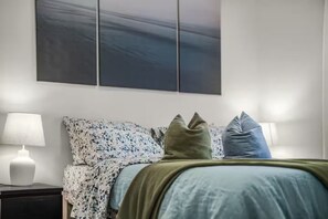 Un dormitorio con una cama, dos lámparas de noche y una obra de arte colgada en la pared.