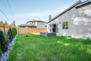 A residential property with a well-maintained lawn, a wooden fence, and a house with a covered patio area. - Cozy Family Home - Fireplace · Backyard · Garage (Vancouver)