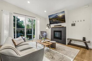 A modern living room with a fireplace, a mounted TV, and a sliding glass door leading to a patio. - Cozy Family Home - Fireplace · Backyard · Garage (Vancouver)