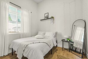 Une chambre à coucher avec un lit, une table de chevet avec une lampe, un miroir et une fenêtre avec des rideaux.