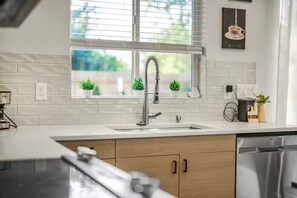 A modern kitchen with a stainless steel faucet, a window with blinds, and a potted plant on the windowsill. - Cozy Family Home - Fireplace · Backyard · Garage (Vancouver)
