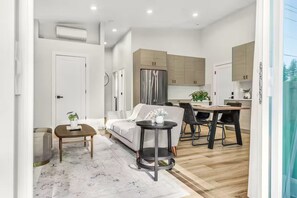 Una sala moderna con un sofá, una mesita redonda y un comedor con sillas.