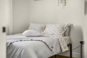A bed with a floral-patterned bedspread and pillows, a bedside table with a lamp, and a hanging plant. - Cozy Family Home - Fireplace · Backyard · Garage (Vancouver)