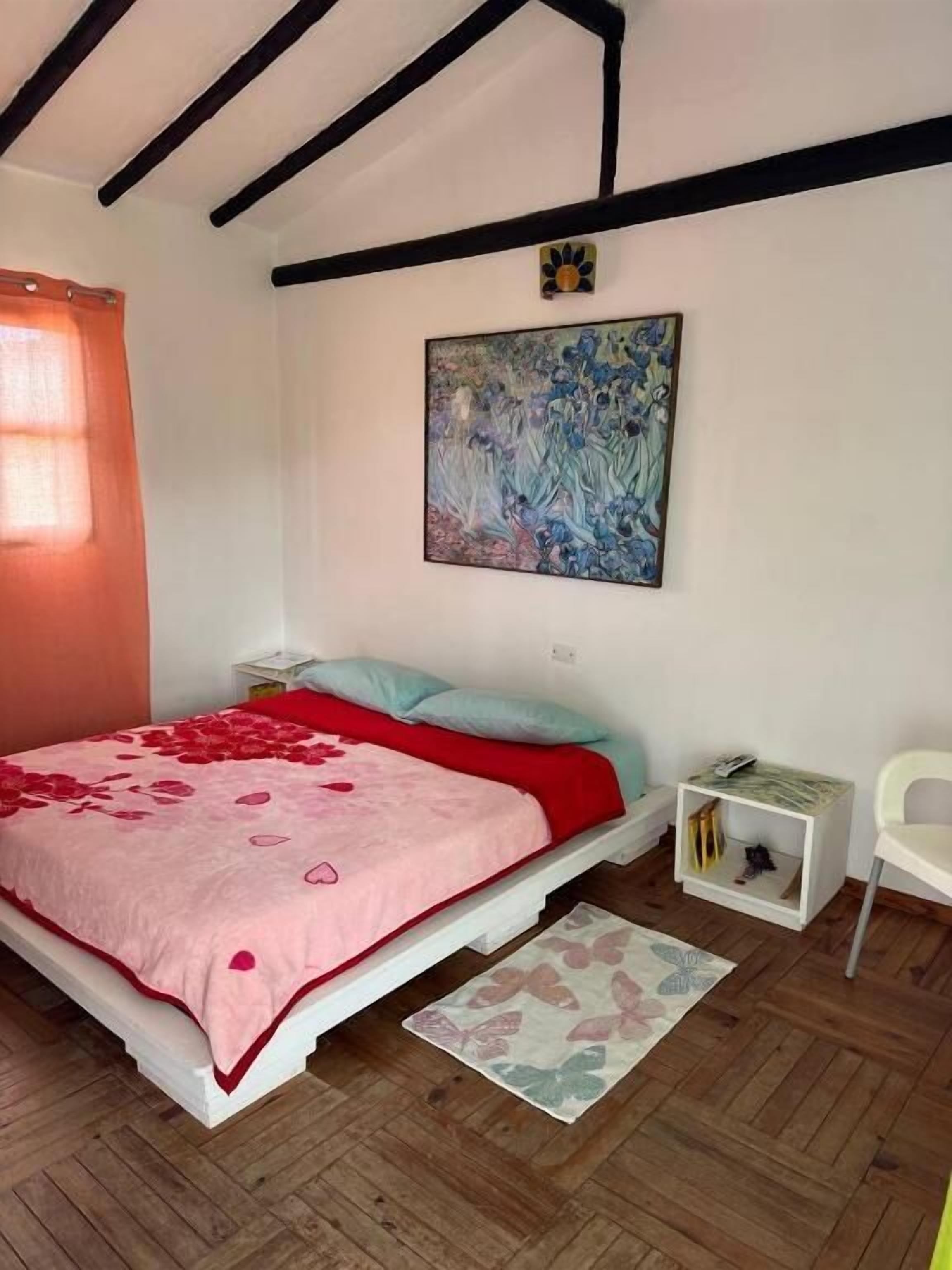 Une chambre à coucher avec un lit, une table de chevet, une chaise, un tableau et un plancher en bois.