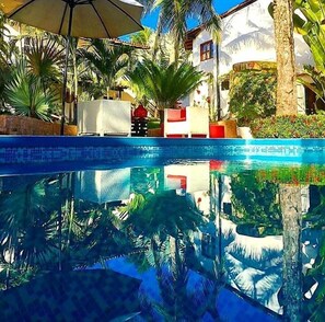 A swimming pool with clear water, surrounded by palm trees and a white building with red accents.