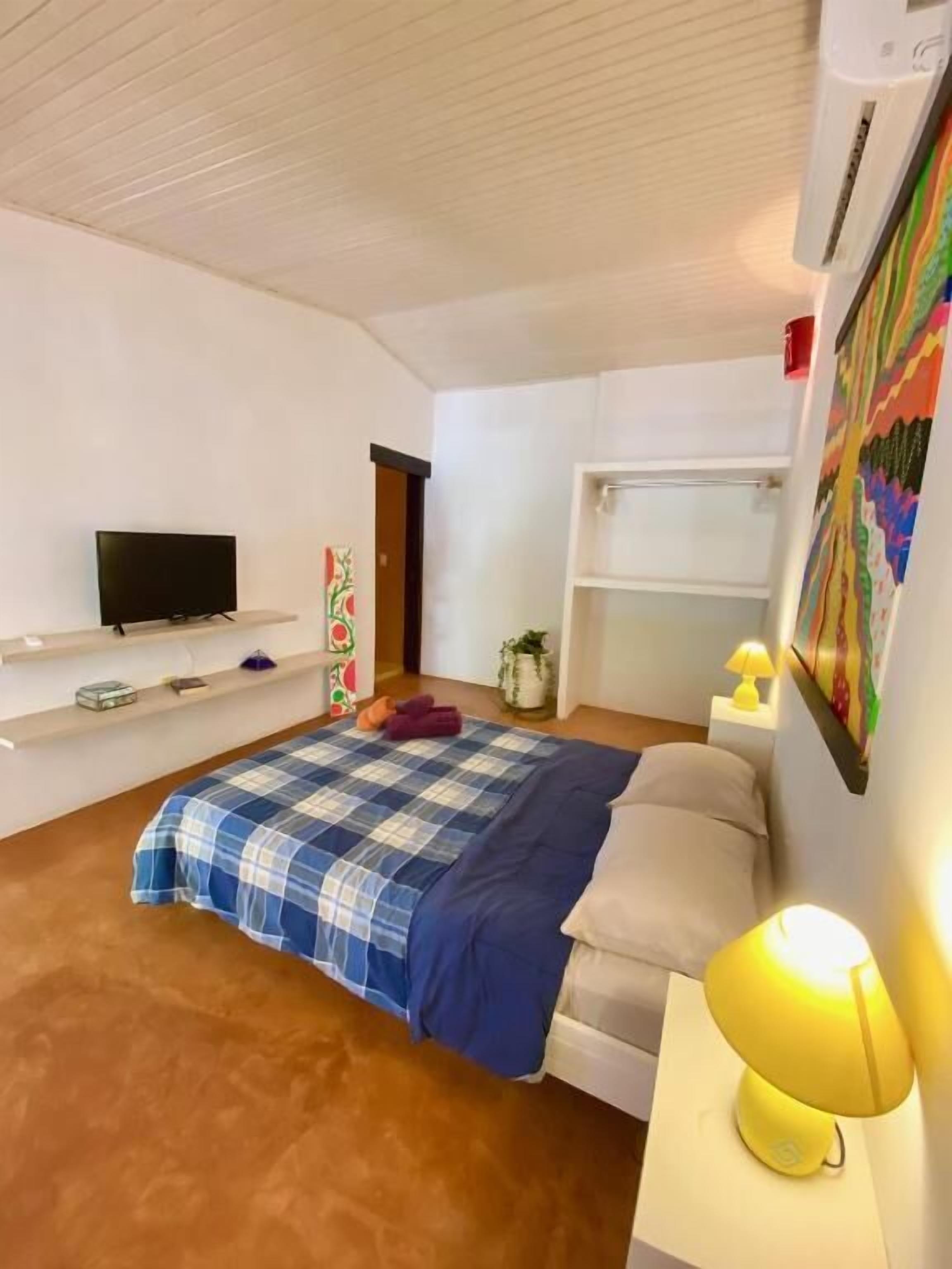A bedroom with a bed, a television, a bedside lamp, and a shelf with items.