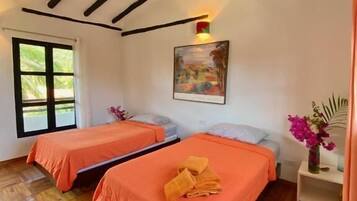 Een kamer met twee bedden, houten vloeren, een schilderij aan de wand en een raam.