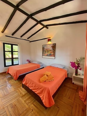 Habitación con dos camas, piso de madera, un cuadro en la pared y una ventana.