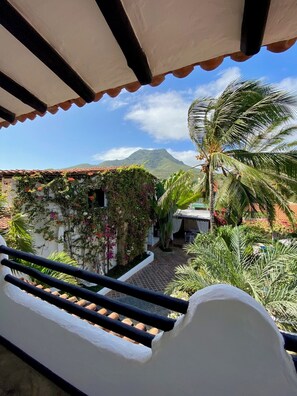 Un balcon avec vue sur une montagne, un palmier et un bâtiment doté d’un toit en tuiles.