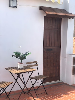 A patio with a wooden table and chairs, a potted plant, and a brown door. - Margarita Penthouse Conil Center – Balcony & Air Conditioning (Conil de la Frontera)