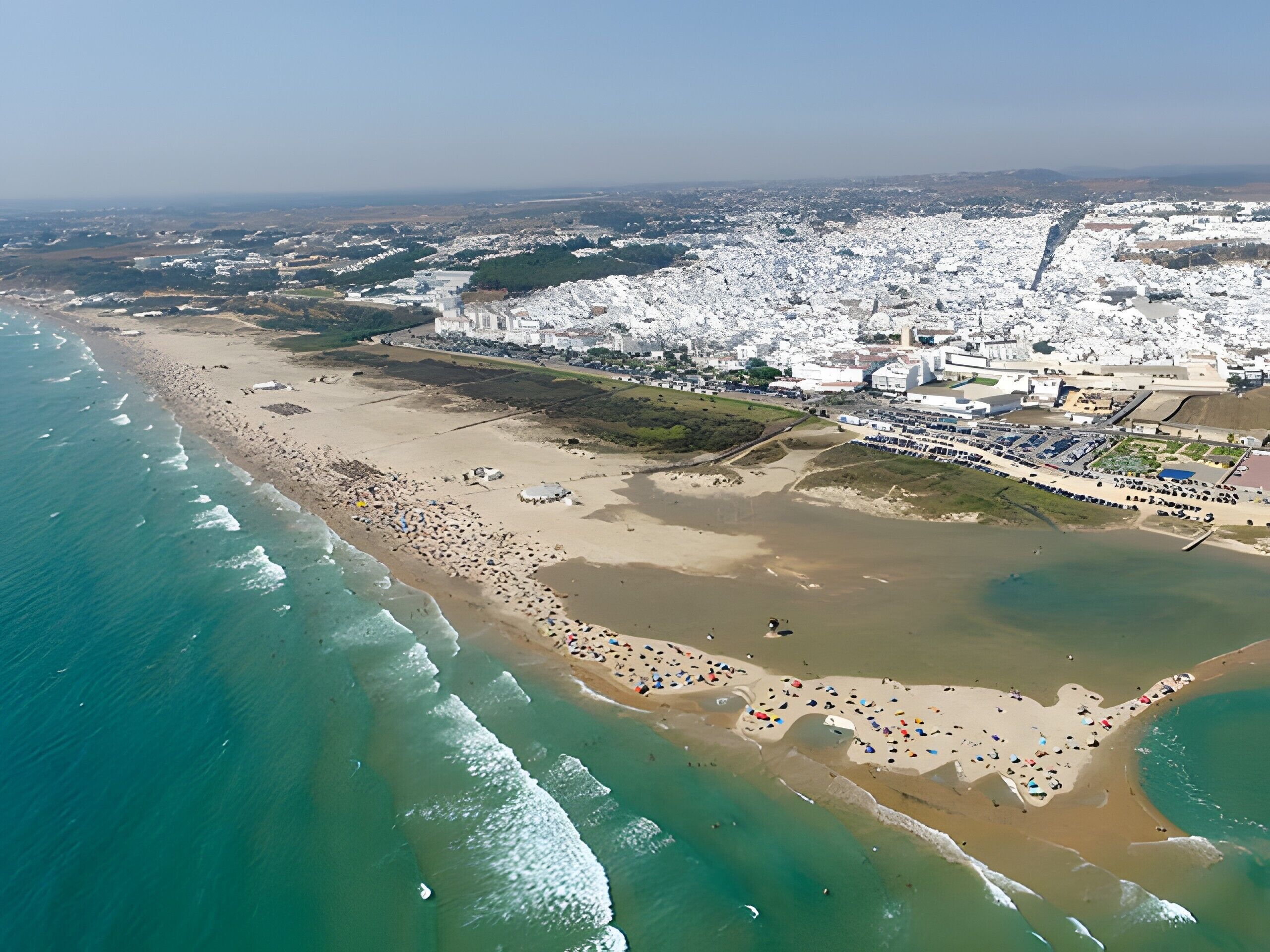 Luftaufnahme einer Küstenstadt mit Strand, Gebäuden und einem Yachthafen.