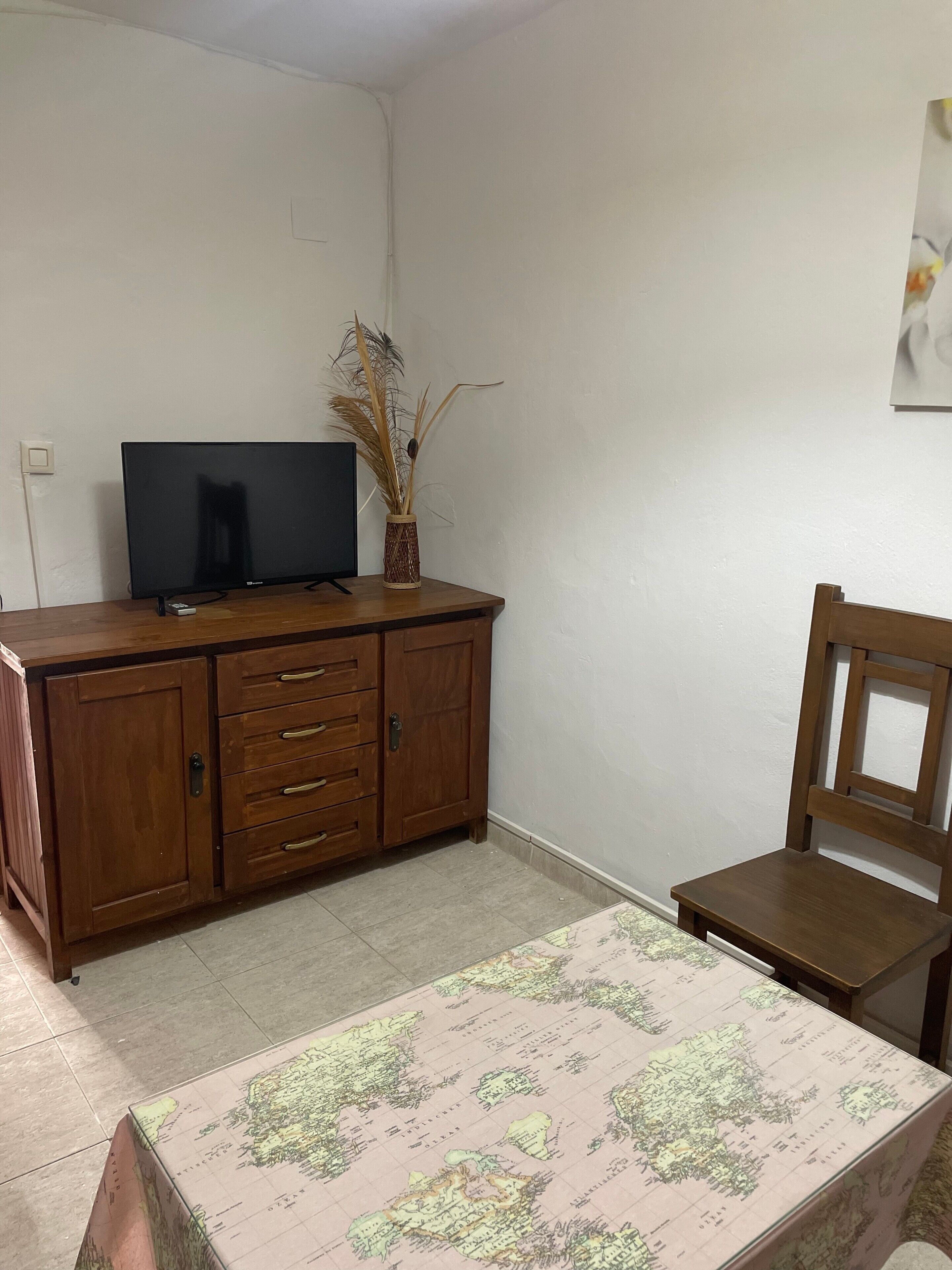 Una habitación con un armario de madera, un televisor, una silla y un mapa en el suelo.