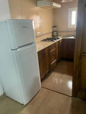 A kitchen with a white refrigerator, wooden cabinets, a gas stove, and a window. - Casa Margarita Conil – Spacious, 3 Bedrooms, Historic Center (Conil de la Frontera)