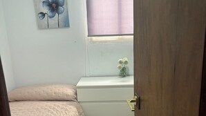Um quarto com cama, cômoda, janela com persiana e um quadro na parede.