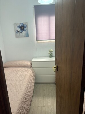 Ein Schlafzimmer mit Bett, Kommode, Fenster mit Jalousie und einem Bild an der Wand.