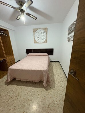 Quarto com cama, ventilador de teto, guarda-roupa e um adorno na parede.