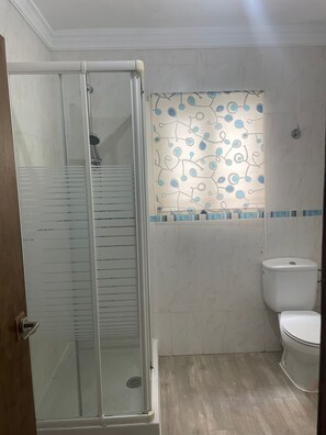 Casa de banho com cabine de duche em vidro, sanita e parede com padrão.