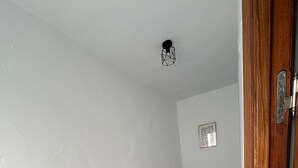 Um quarto pequeno e estreito com uma cama, um banco de madeira e uma porta.