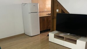 Um quarto pequeno com uma geladeira branca, um armário de madeira e uma televisão sobre um suporte branco.
