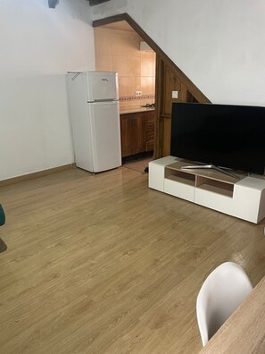 Ein kleines Zimmer mit einem weißen Kühlschrank, einem Holzschrank und einem Fernseher auf einem weißen Schrank.