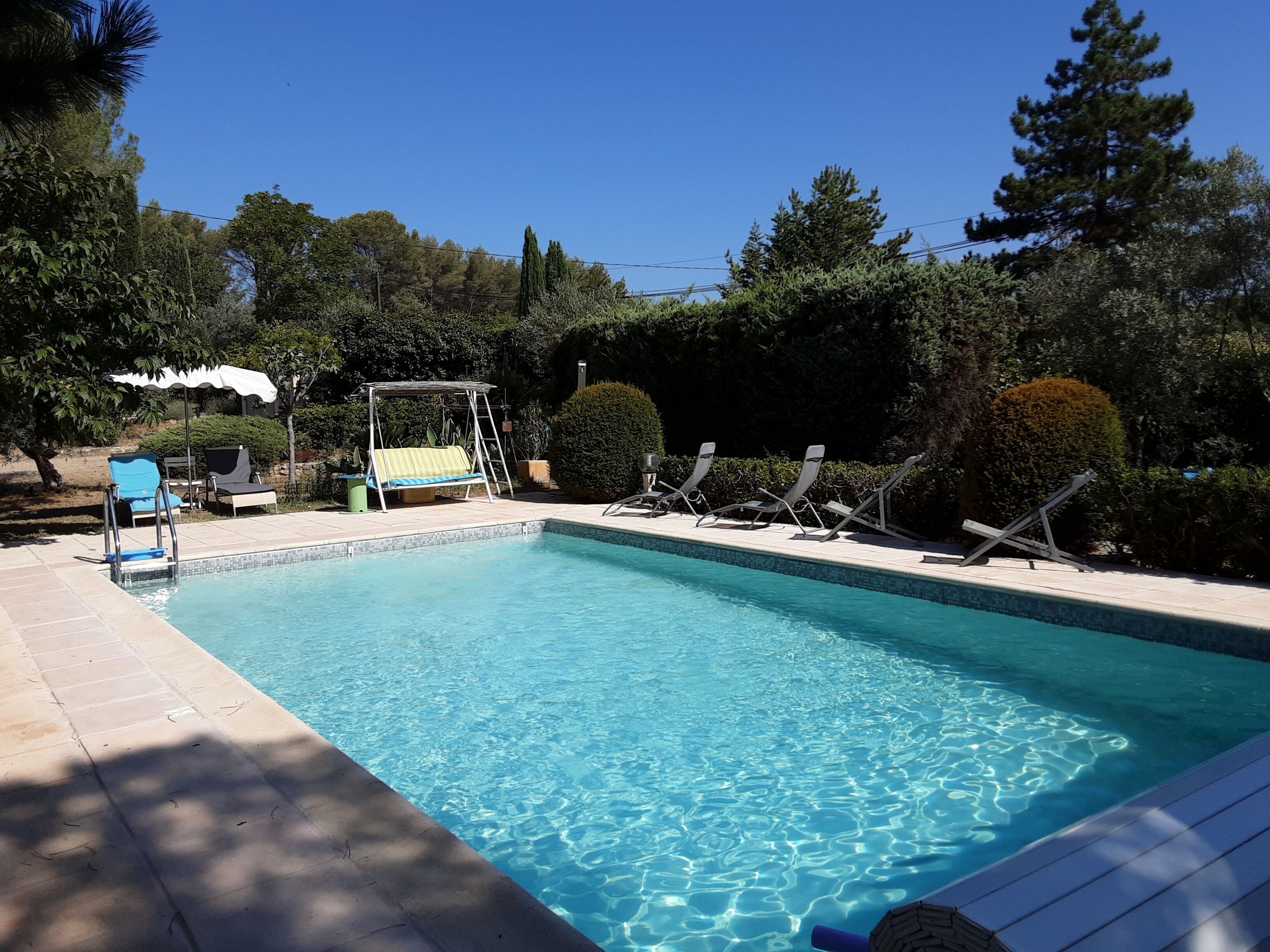 A clear blue swimming pool with lounge chairs and a sunbed.