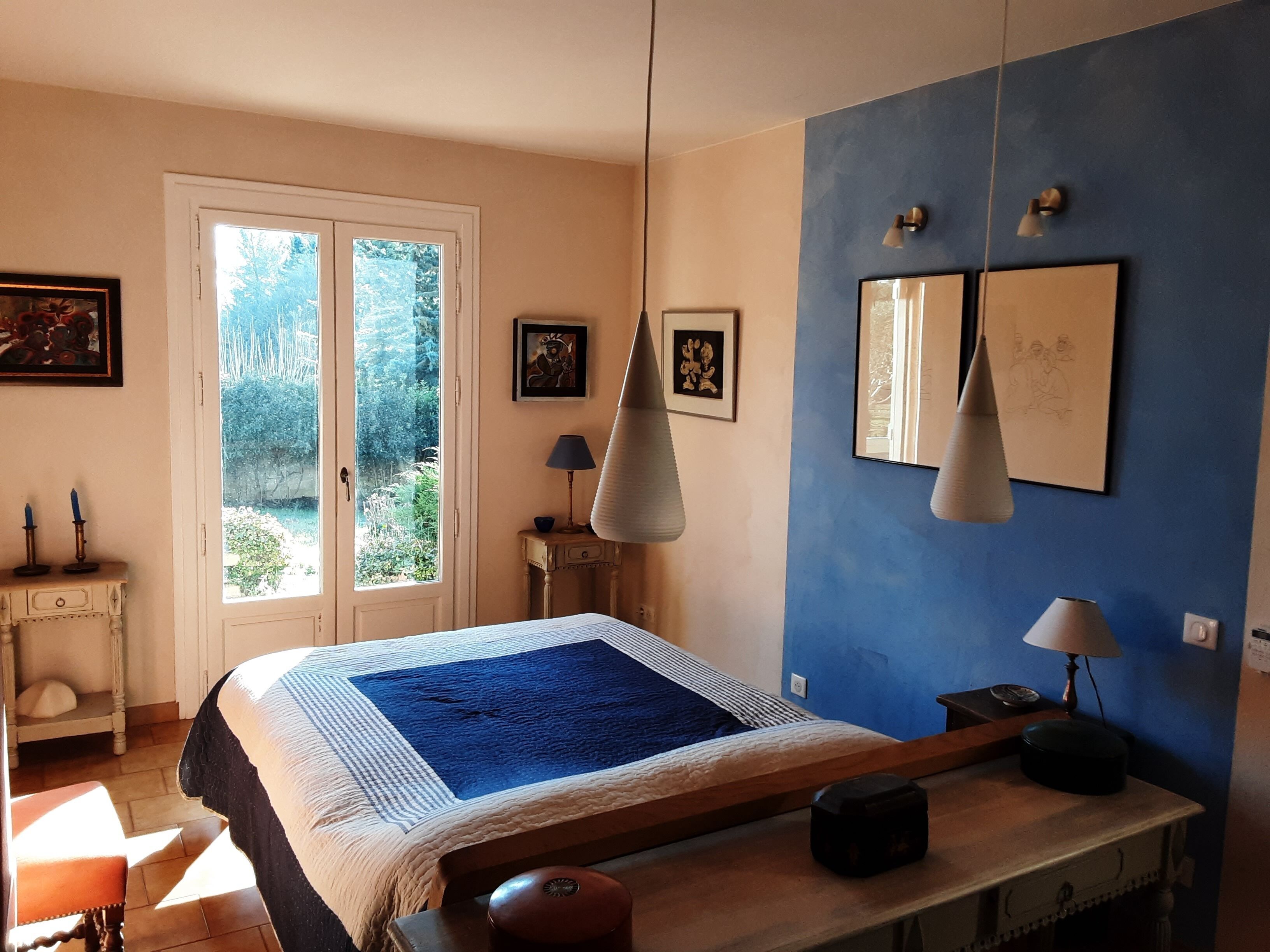 A bedroom with a bed, bedside table, lamp, and a view through a door.